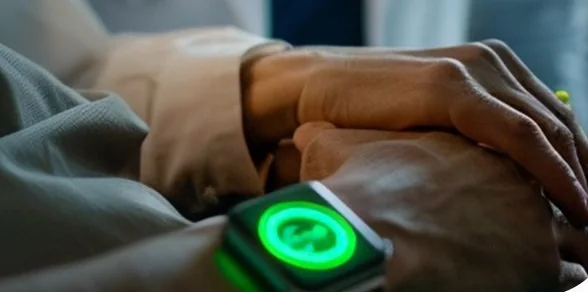 A person's wrist resting on their arm, wearing a sensor that glows green